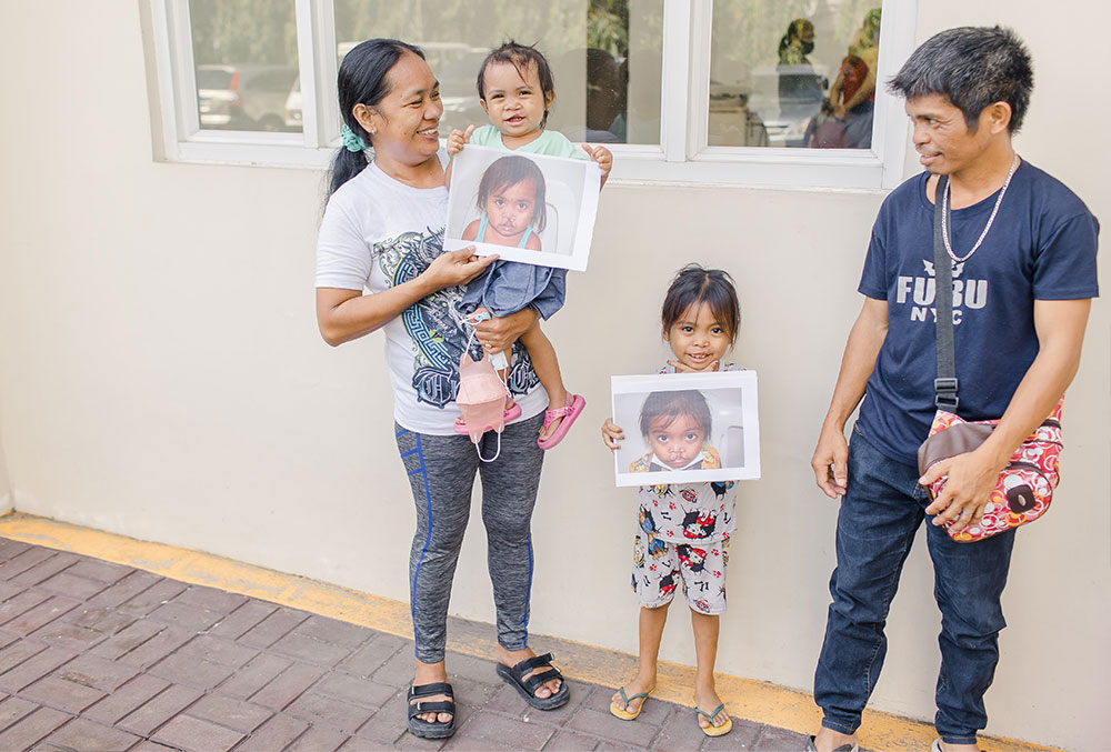 Pacatang family smiling and holding pictures of themselves before cleft surgery