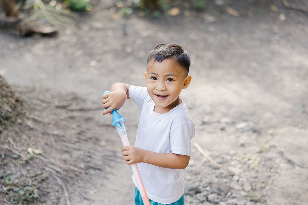 Emmanuel smiles and holds a toy for blowing bubbles