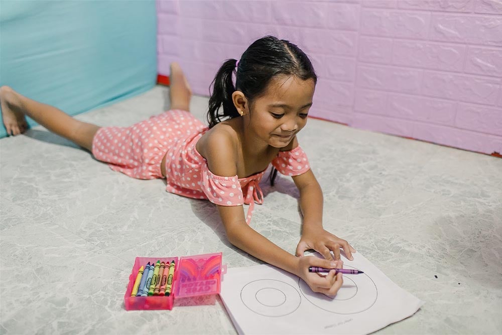 Leana laying on the floor coloring a coloring sheet with crayons